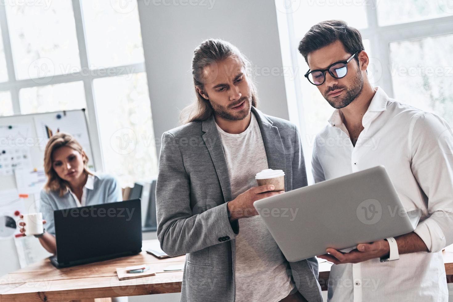 Working as a team. Two young modern men in smart casual wear using laptop while working in the creative office photo