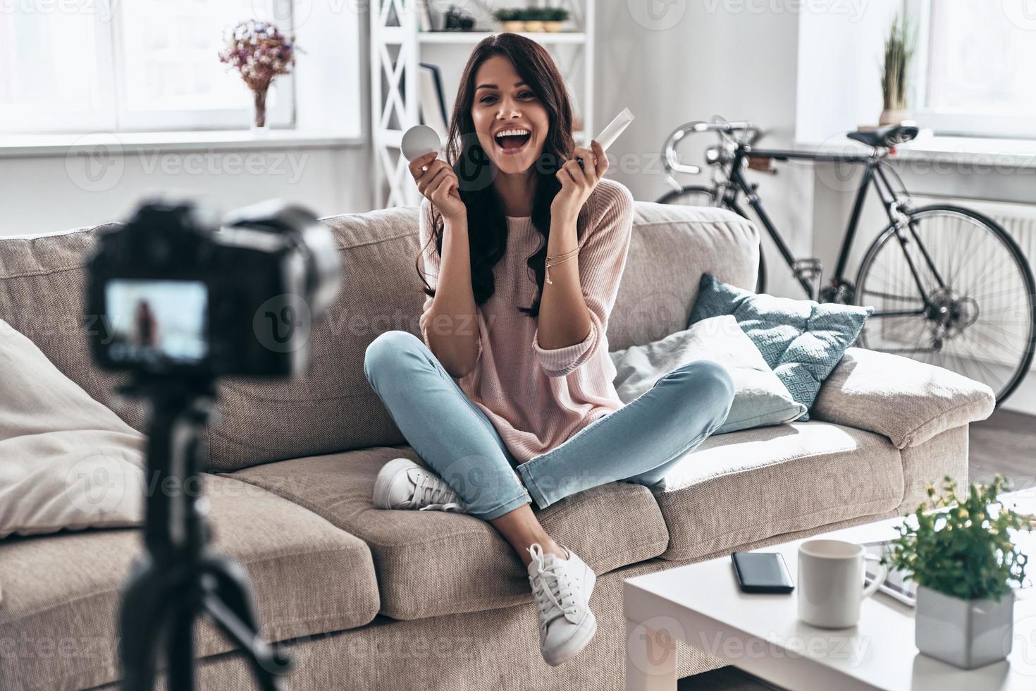 Another video in her vlog. Beautiful young woman holding beauty products and smiling while making social media video photo