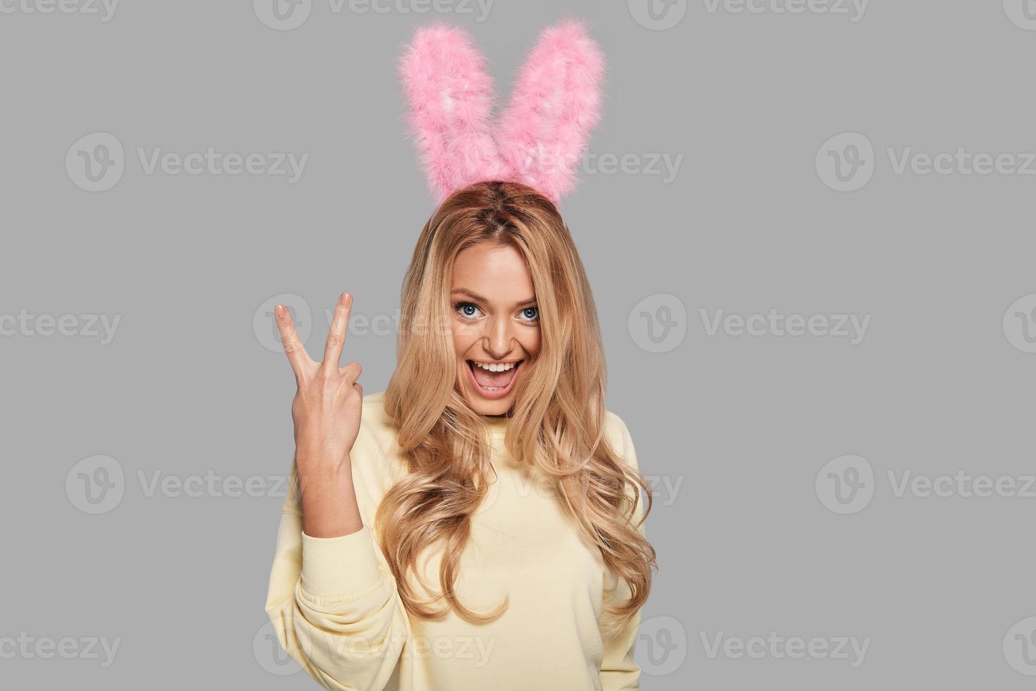 Staying cool. Attractive young smiling woman in pink bunny ears gesturing and looking at camera while standing against grey background photo