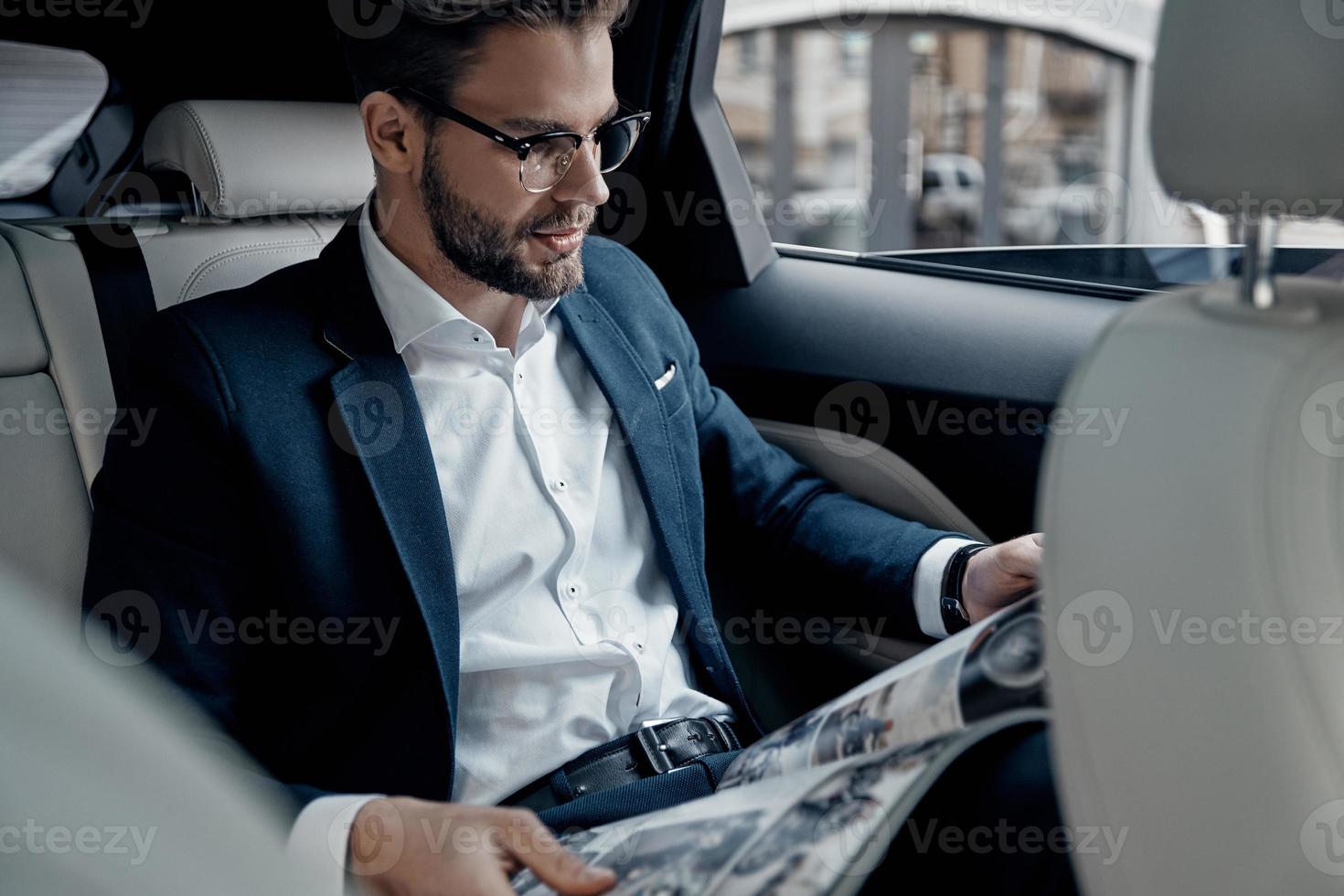 Handsome young man in full suit reading a newspaper while sitting in the car photo