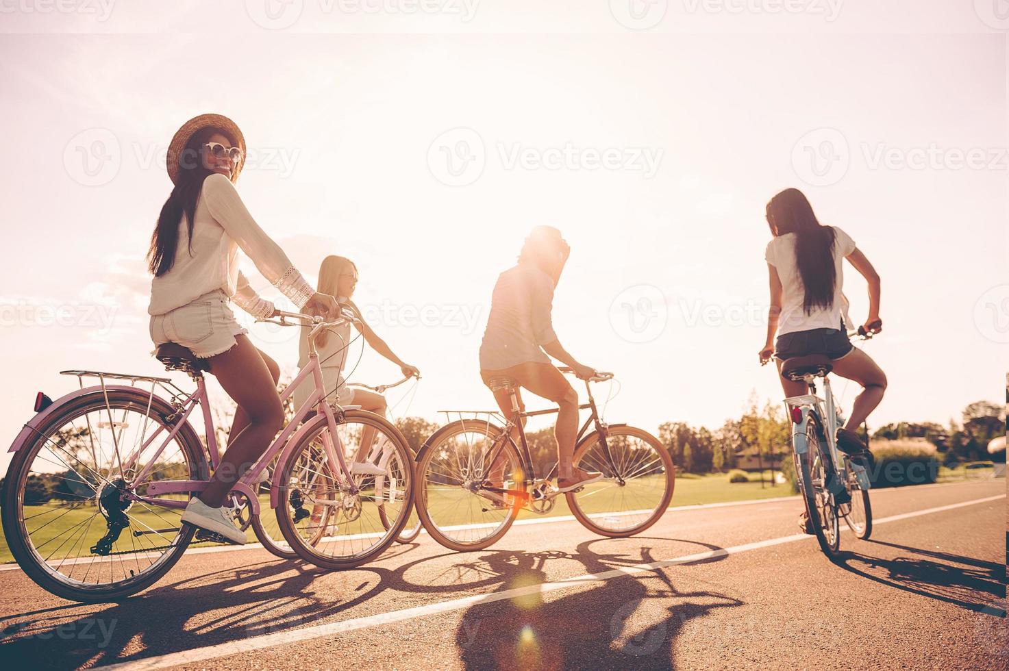 Perfect day for cycling. Low angle view of young people riding bicycles along a road and looking happy photo