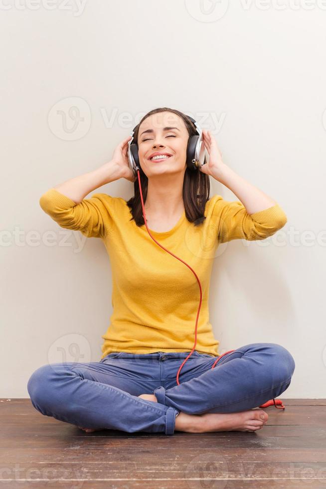 disolviéndose en una música encantadora. bella joven con auriculares manteniendo los ojos cerrados mientras se sienta en el suelo contra el fondo marrón foto