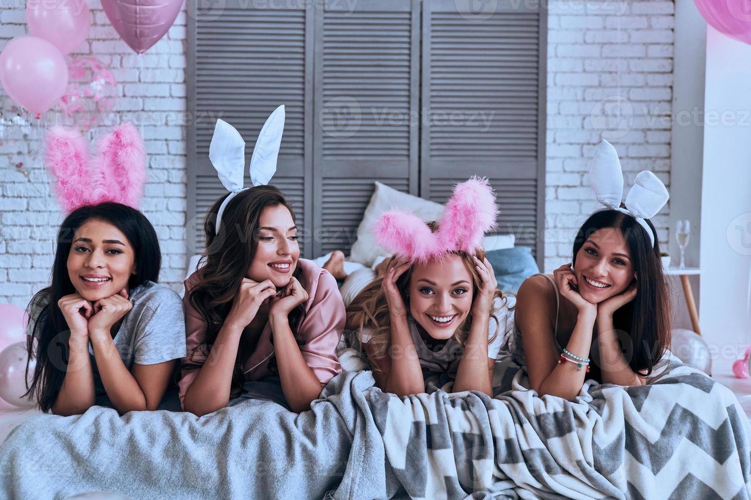 Funny bunnies. Four playful young women in bunny ears smiling while lying on the bed photo