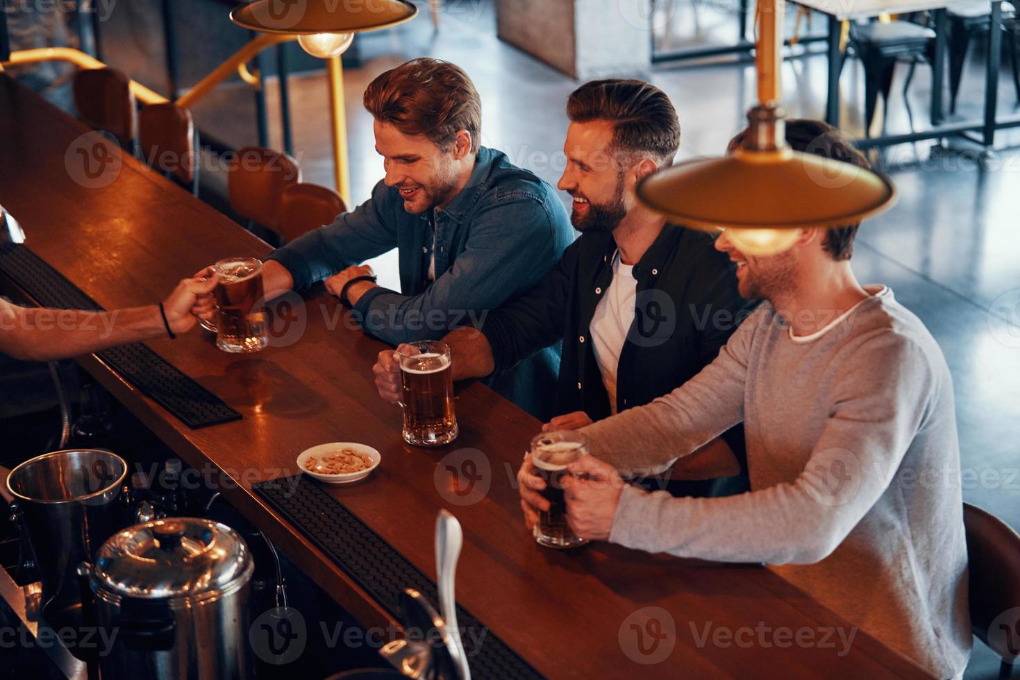 Top view of bartender serving beer to young men while standing at the bar counter in pub photo