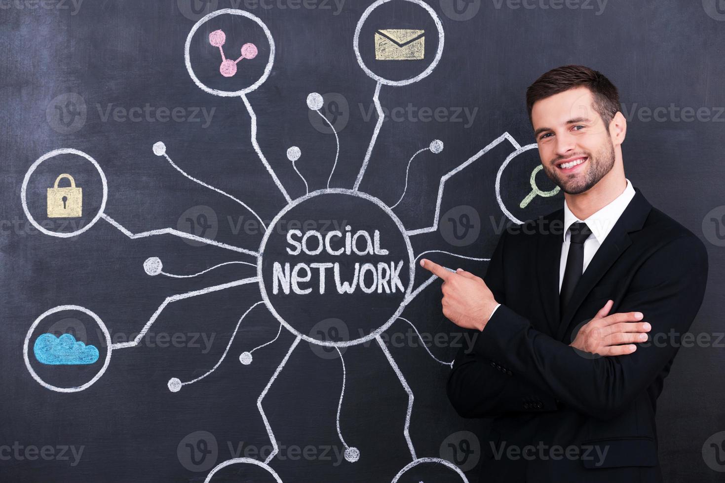 Social network. Handsome young man standing against social network chalk drawing on blackboard and pointing on it photo