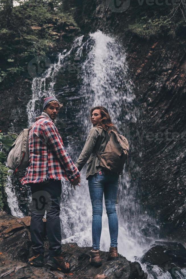 Getting away from it all... Full length rear view of young couple holding hands while standing near the waterfall photo