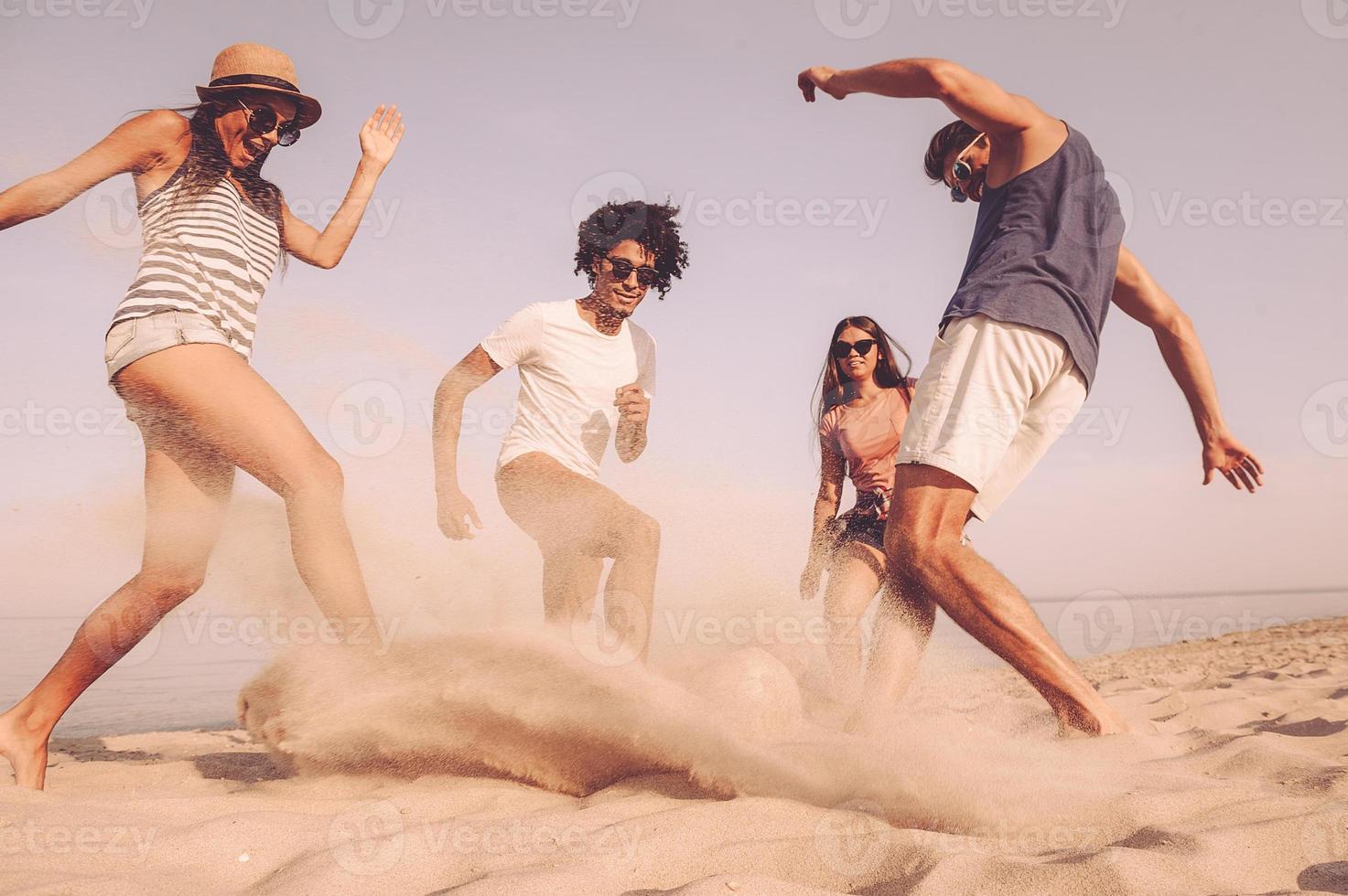 Beach soccer with friends. Group of cheerful young people playing with soccer ball on the beach photo