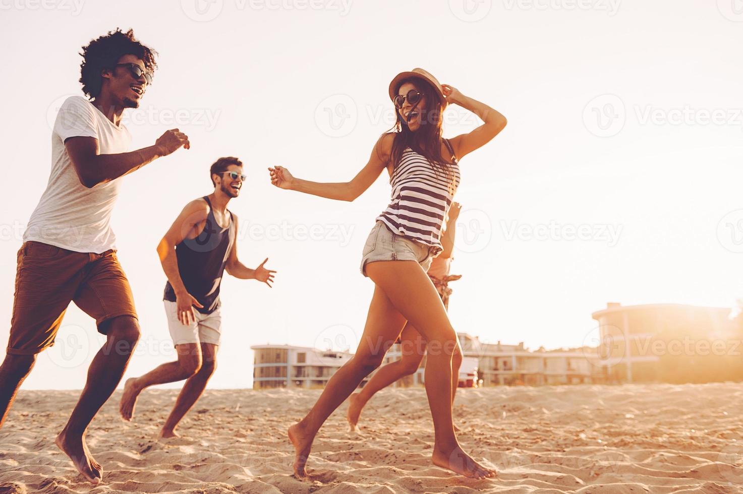 They love having fun. Group of young cheerful people running along the beach and looking happy photo