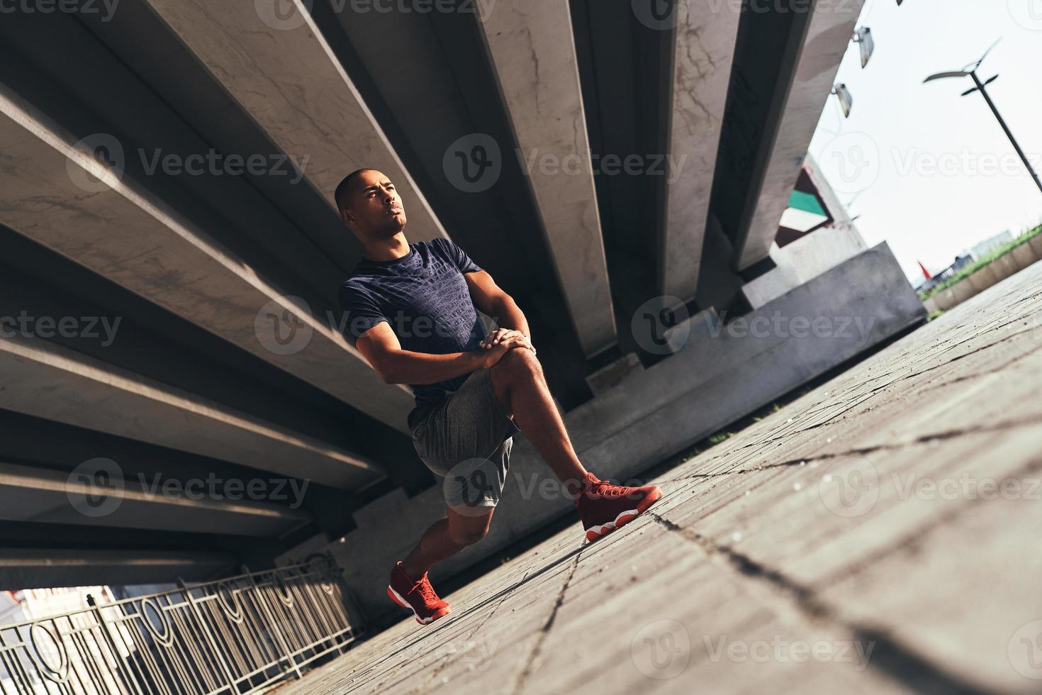 Warming up. Handsome young African man in sports clothing stretching while warming up outdoors photo