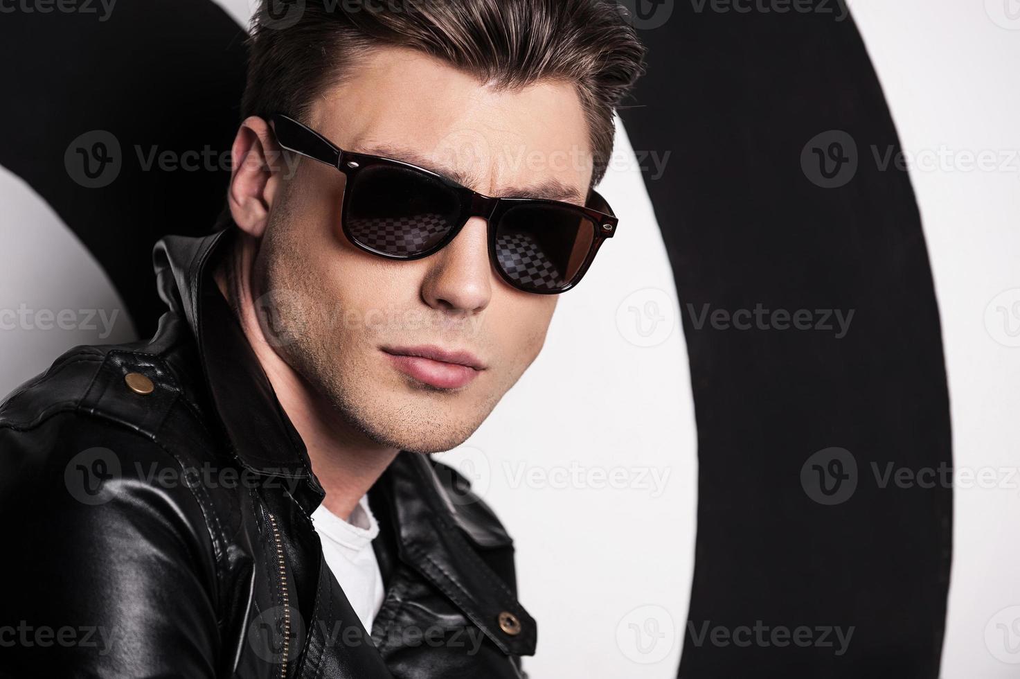 Cool and handsome. Handsome male model in leather jacket standing against target background and looking at camera photo