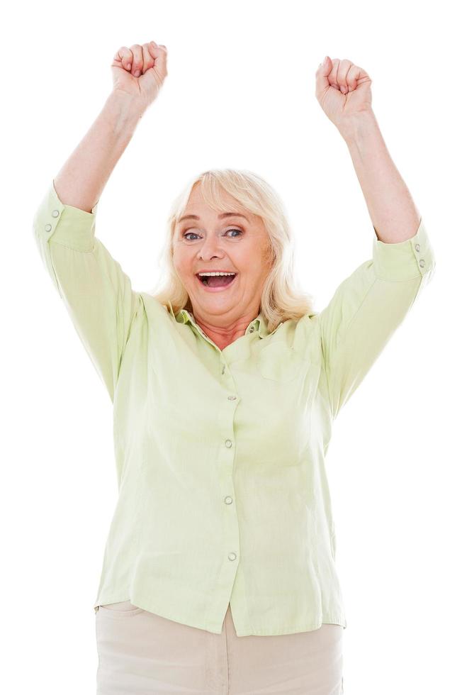 Happy winner. Happy senior woman keeping arms raised and looking at camera while standing isolated on white background photo
