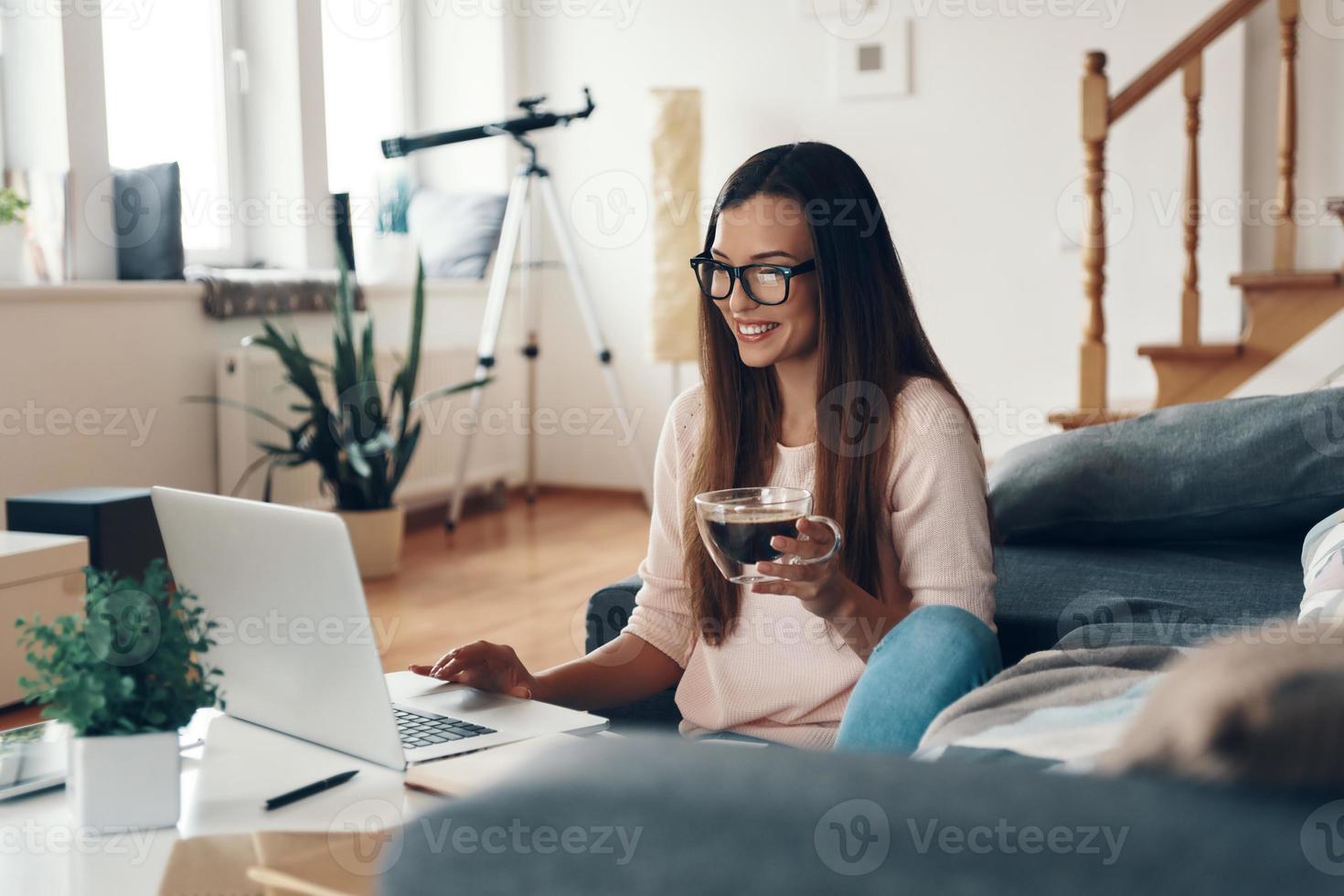 Happy young woman in casual clothing using laptop and smiling while resting at home photo