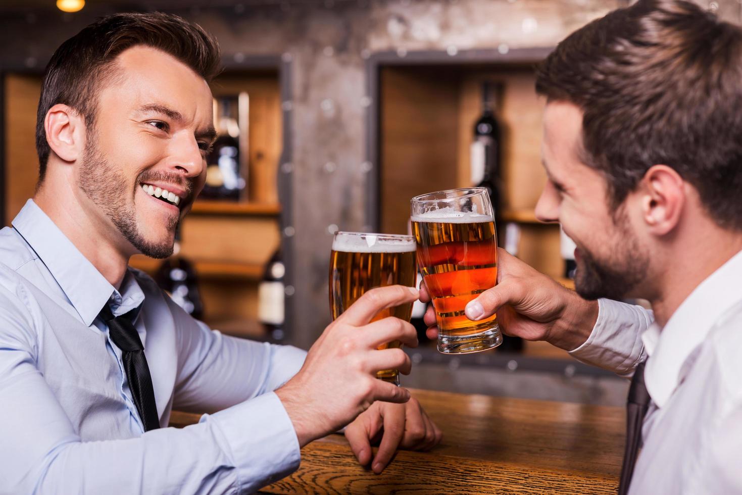 Having a pint with friend. Two cheerful young men in shirt and tie
