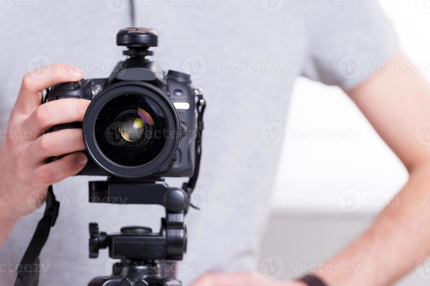 Ready to shoot. Close-up of man holding digital camera while standing in studio with lighting equipment on background photo