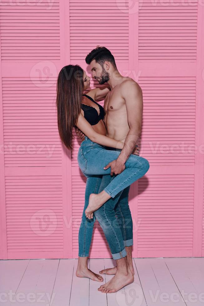 Beauty and style. Full length of beautiful young couple bonding face to face while standing against pink background photo