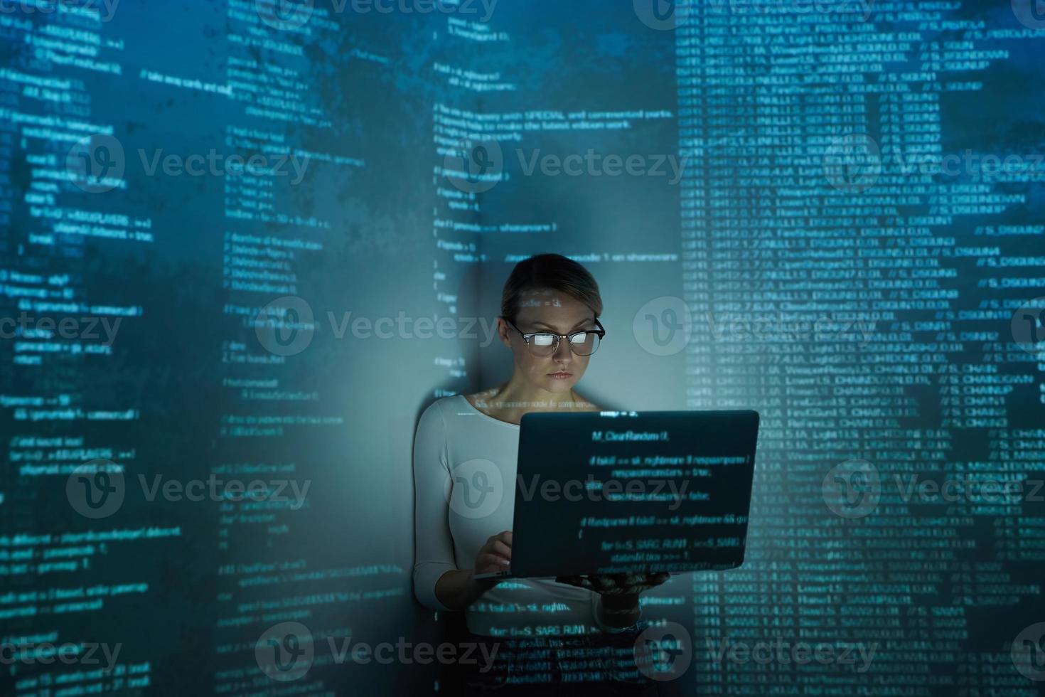 Confident young woman using computer against dark background photo