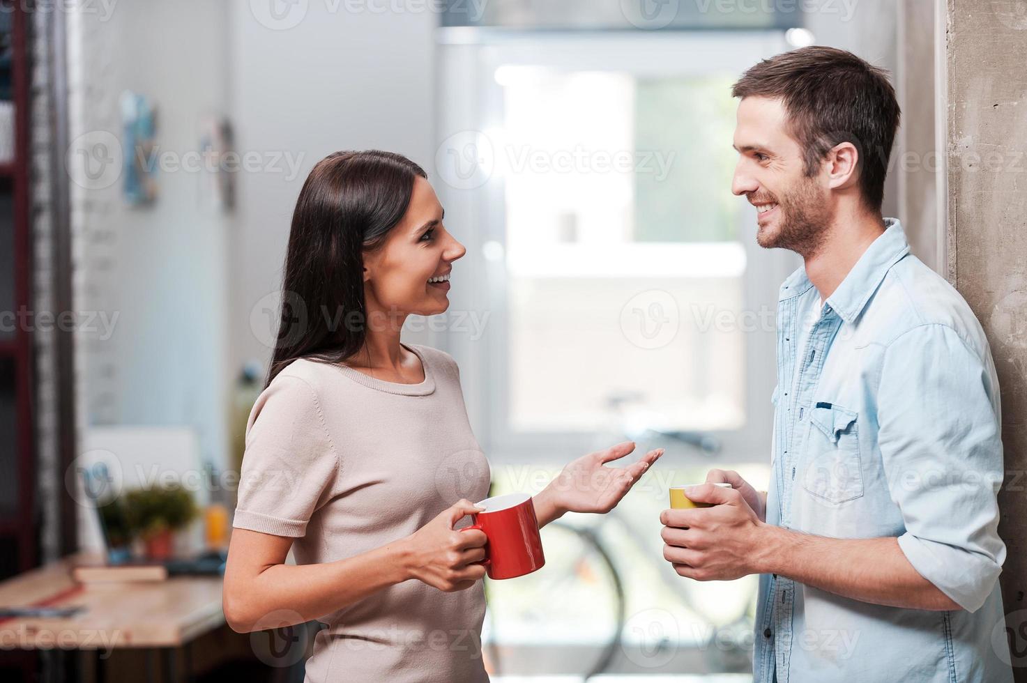 pasando un buen descanso para tomar café. dos jóvenes alegres sosteniendo tazas de café y hablando mientras están en el cargo foto