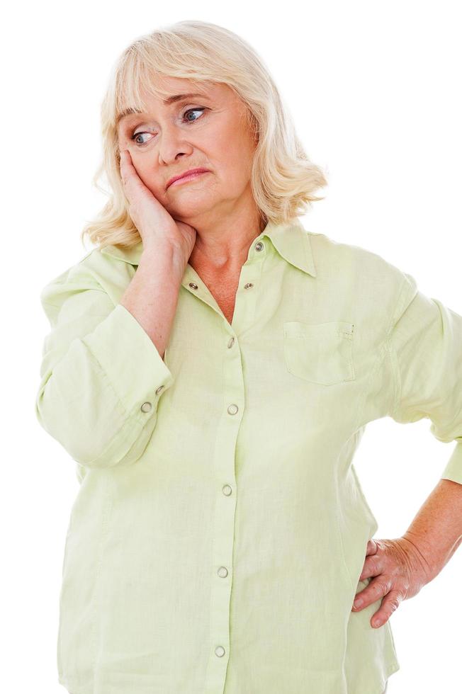 Depressed senior woman. Depressed senior woman leaning her face on hand and looking away while standing isolated on white background photo