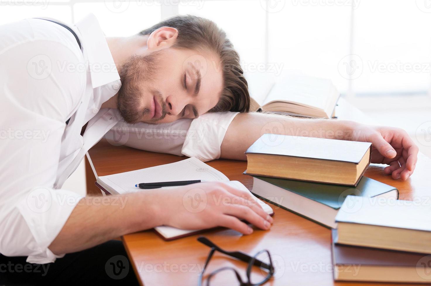 Tired after night of research. Rear view of thoughtful young man in shirt and suspenders sitting on the table and reading a book laying on it photo