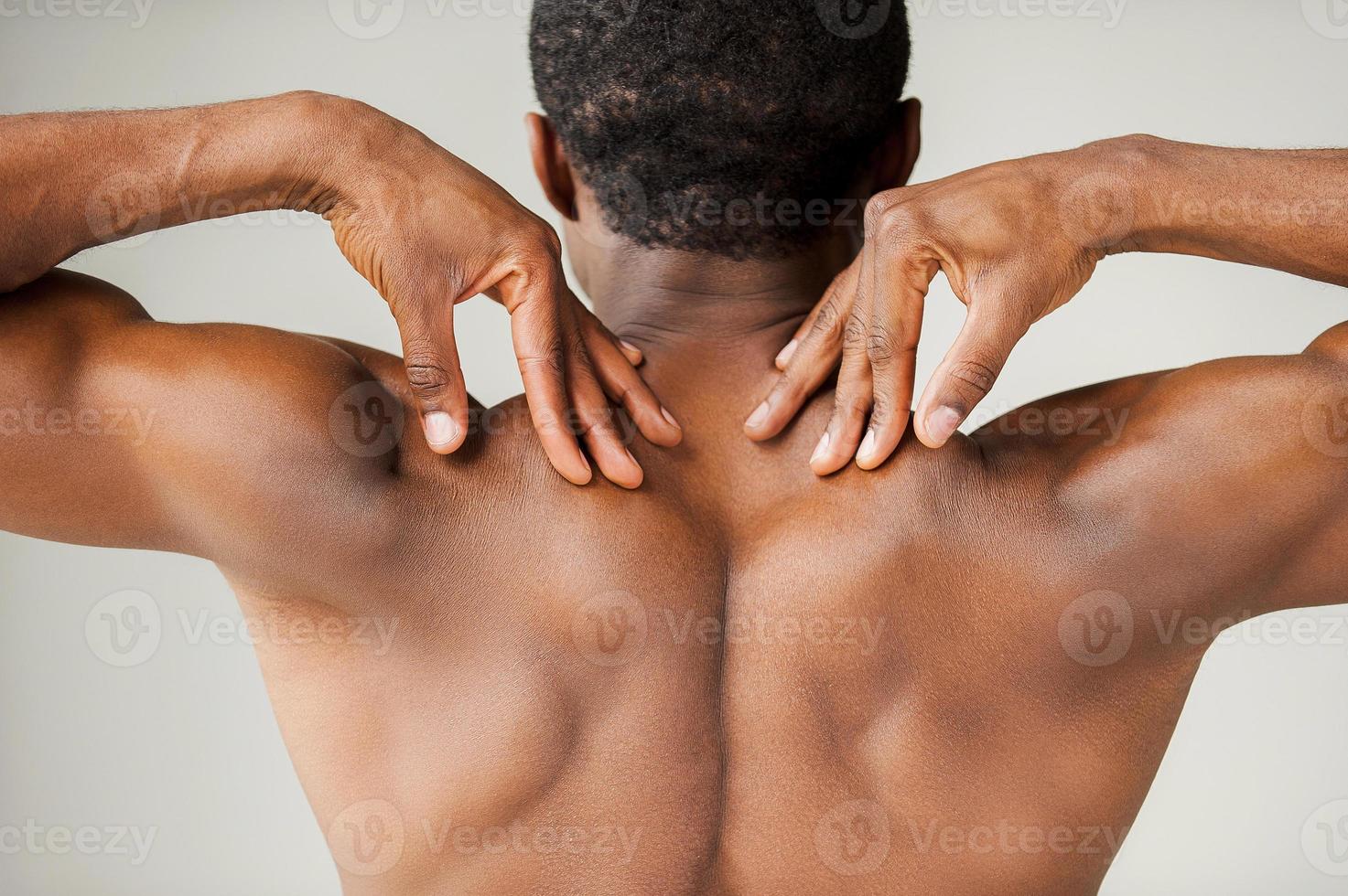 Muscular black man. Rear view of young muscular black man touching his shoulders while standing isolated on grey background photo