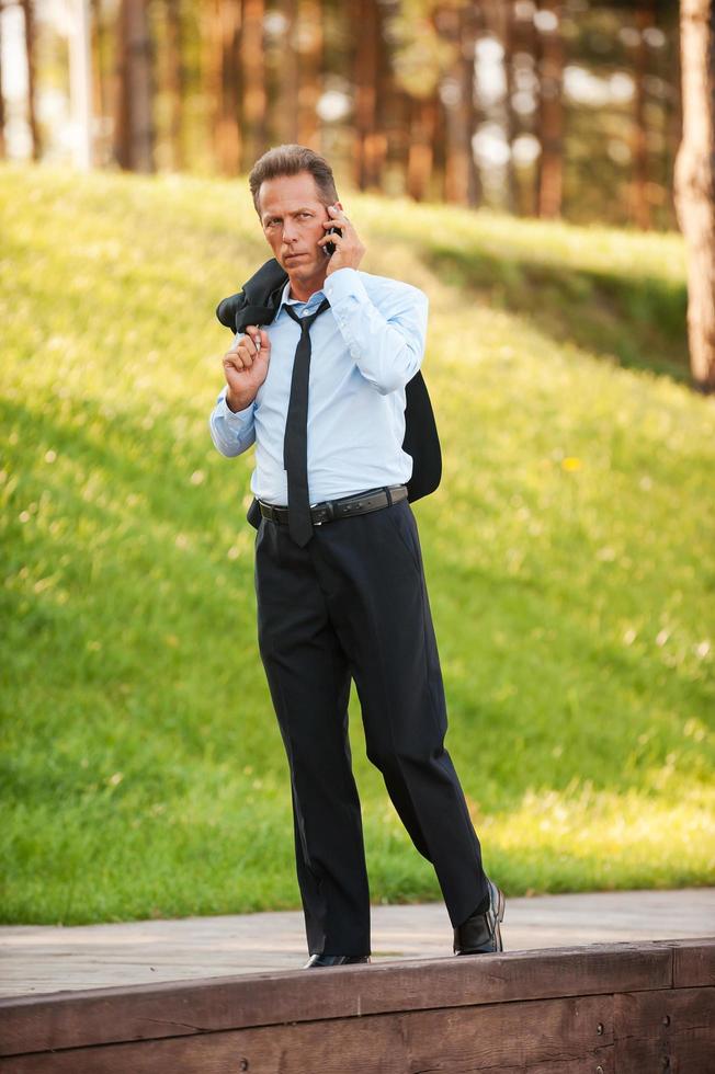 Always staying connected. Serious mature businessman talking on the mobile while walking in park photo