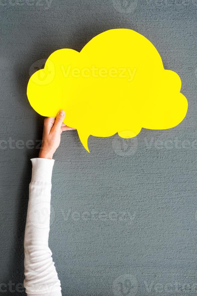 Cloud for your advertisement. Close-up of woman stretching out empty speech bubble against grey background photo