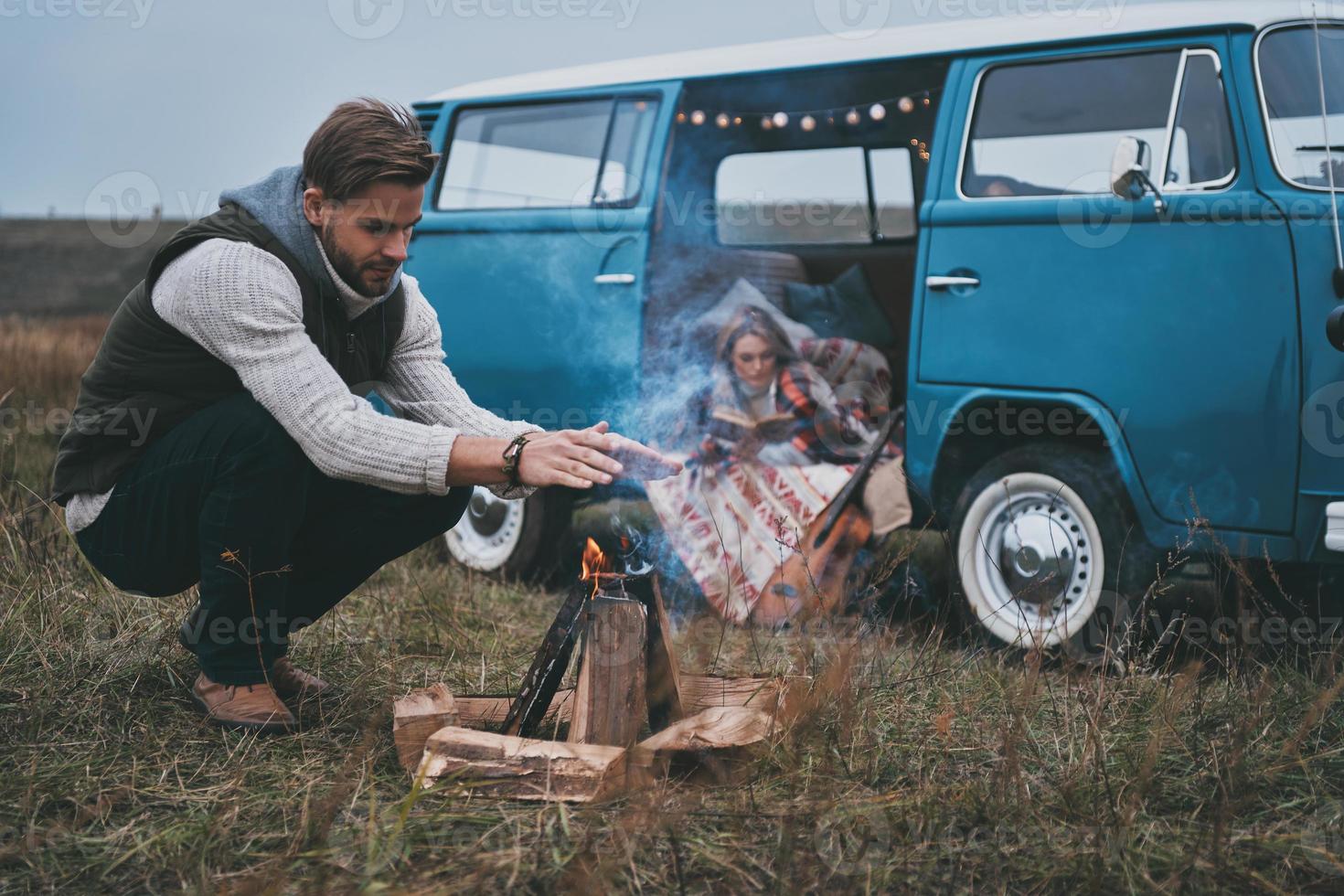 Best way to keep you warm.  Beautiful young woman reading a book while her boyfriend warming up by the bonfire photo