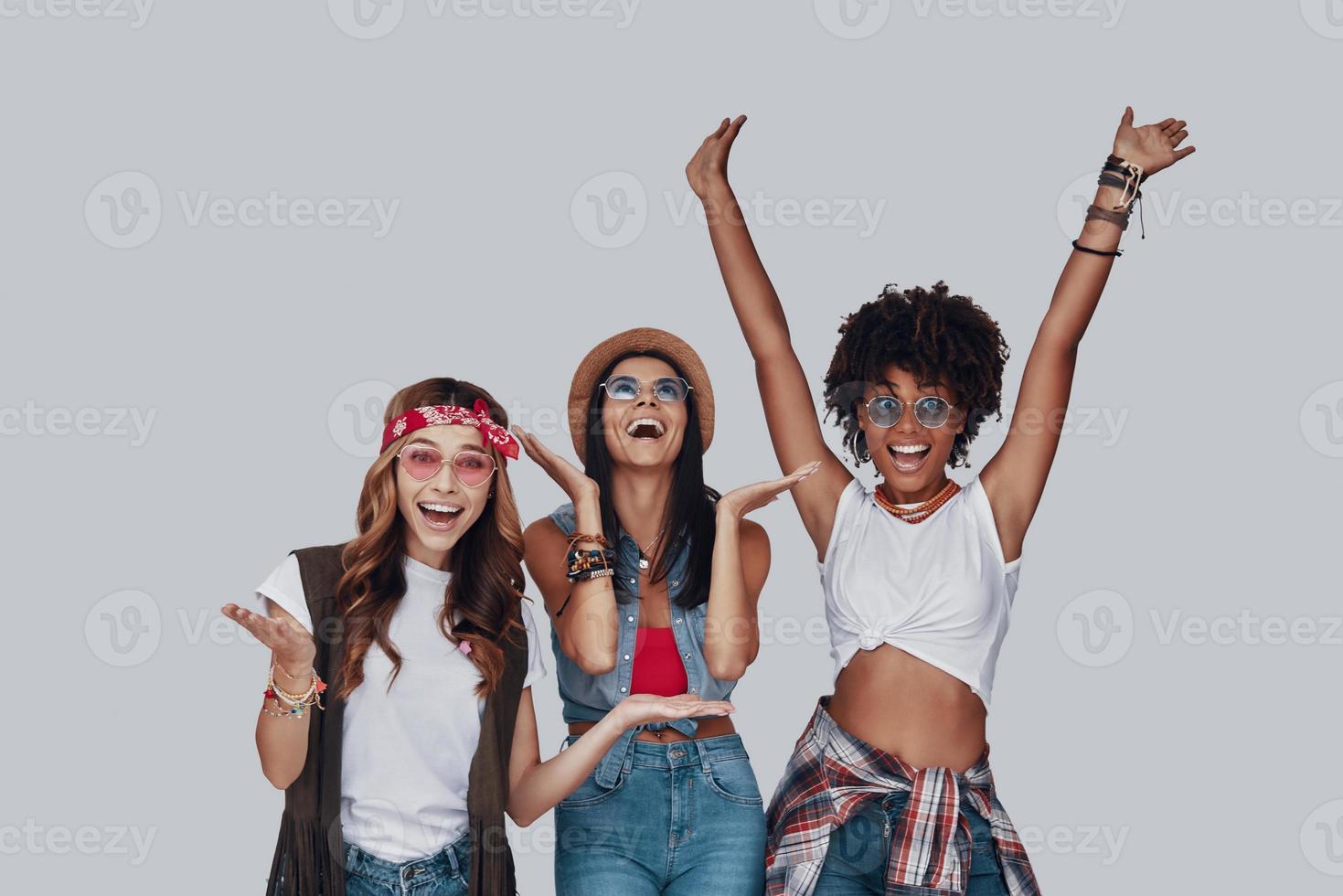 Three attractive young women cheering and smiling while standing against grey background photo