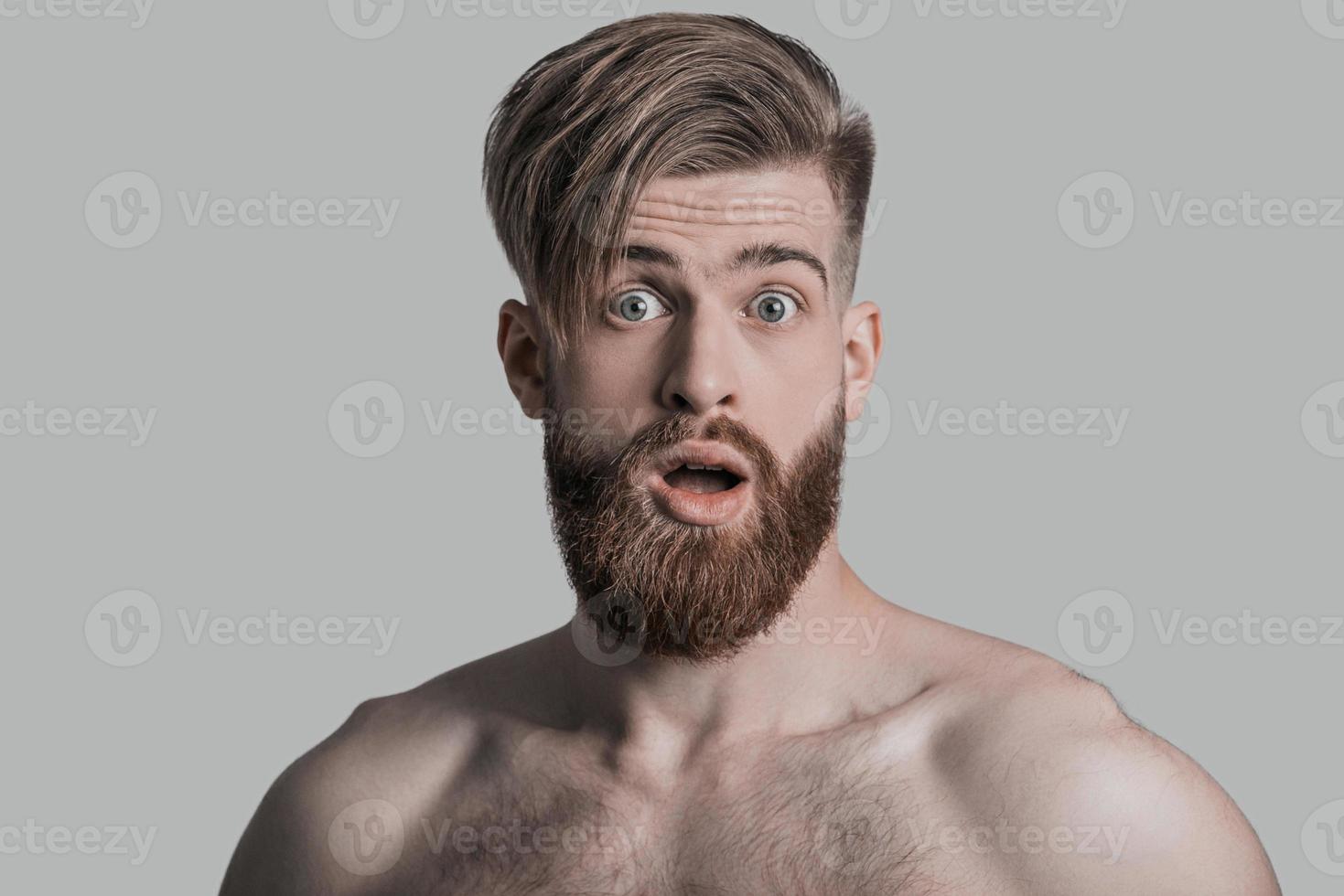 Portrait of young man looking at camera with opened mouth while being in front of grey background photo