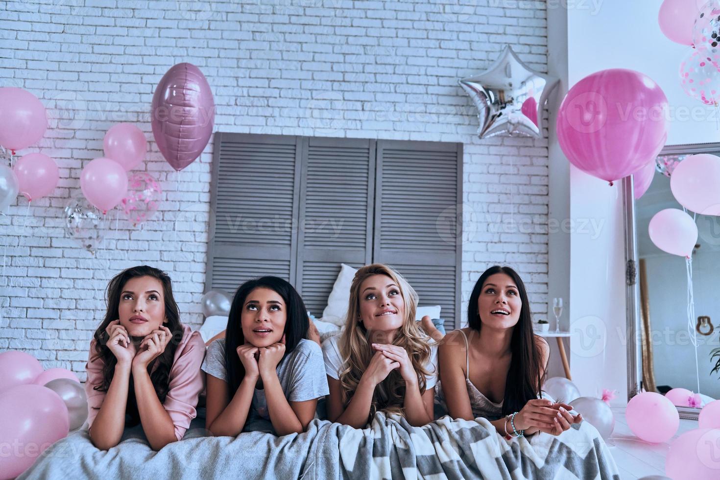 Thinking about Four beautiful young women in pajamas looking away while lying on the bed photo