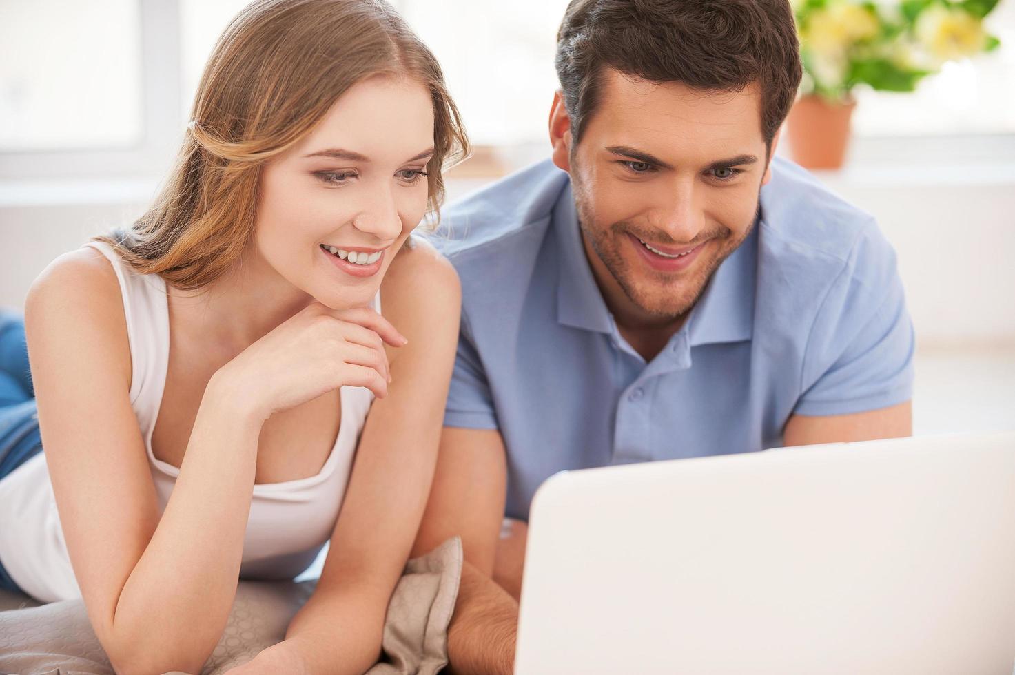 Spending their free time in the net. Cheerful young couple surfing the net together while lying on the floor and looking at the laptop photo