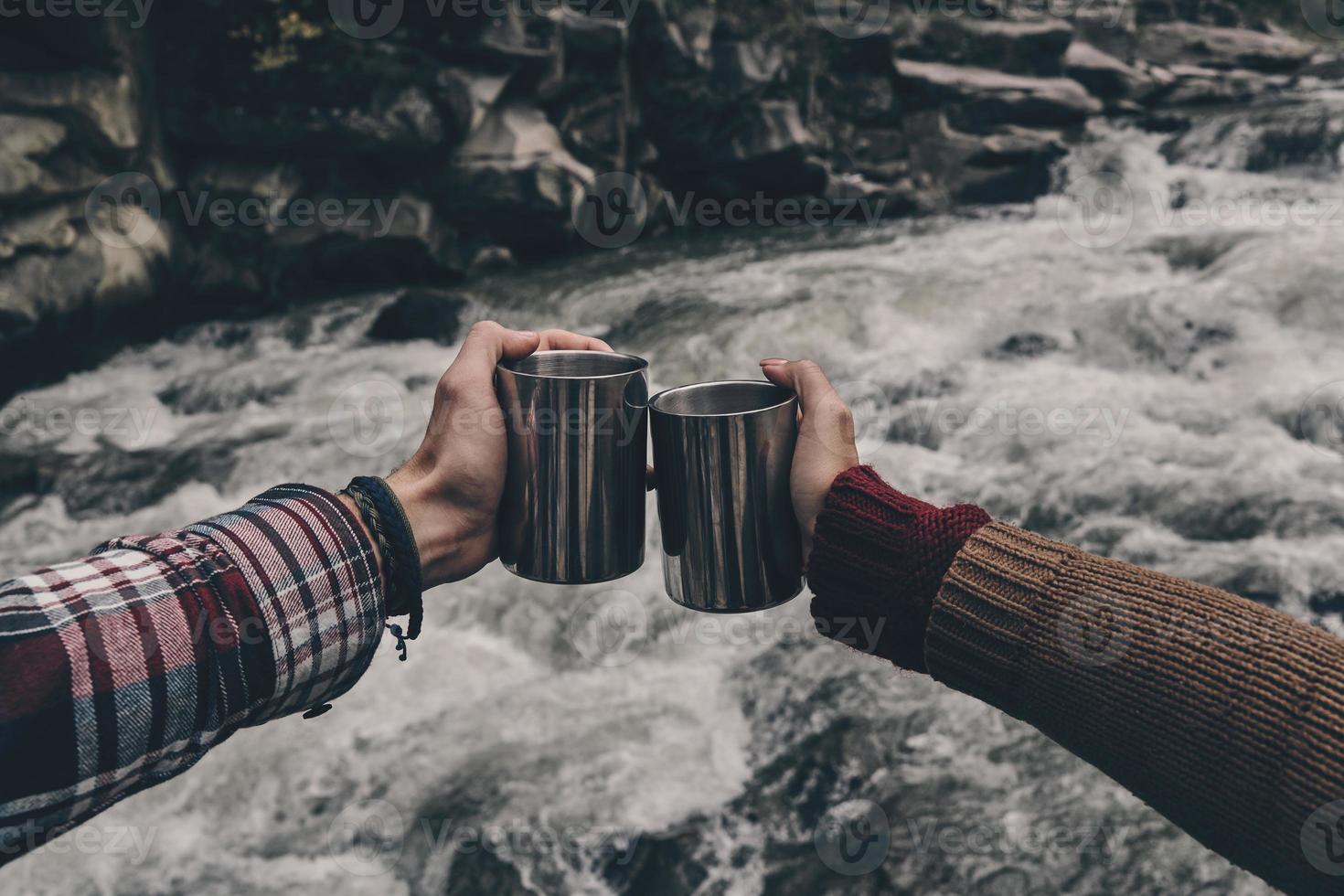 Close up of young couple toasting each other while relaxing on the rocks near the river photo