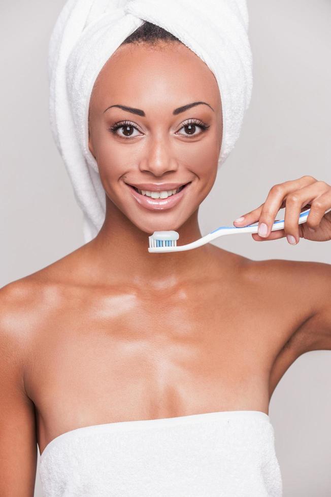 Teeth care. Portrait of beautiful young Afro-American woman holding a toothbrush and looking at camera while standing against gray background photo