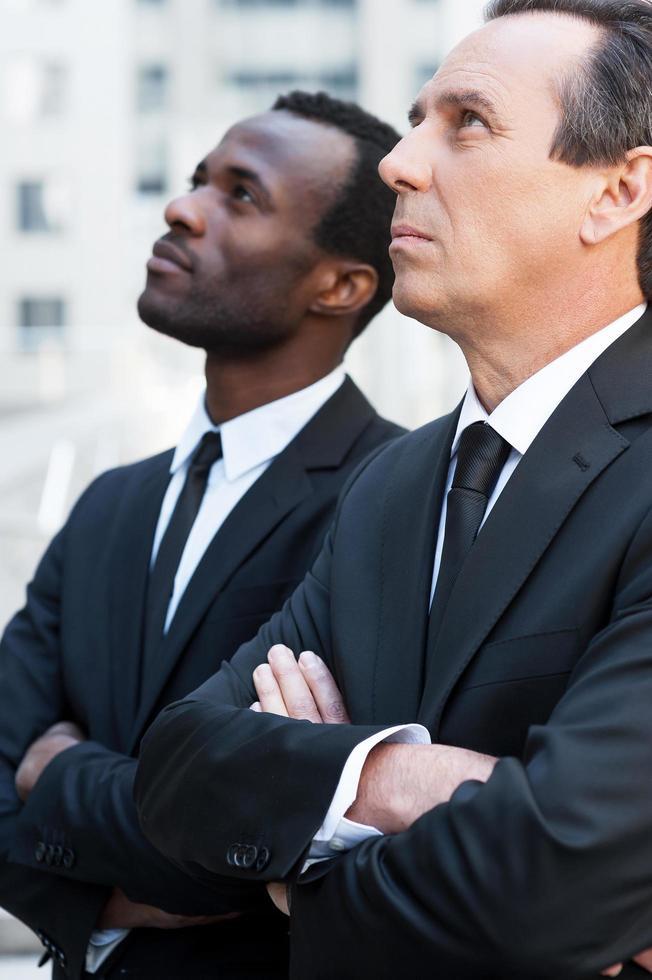 Looking for new solutions. Side view of two confident businessmen keeping arms crossed and looking up while standing outdoors photo