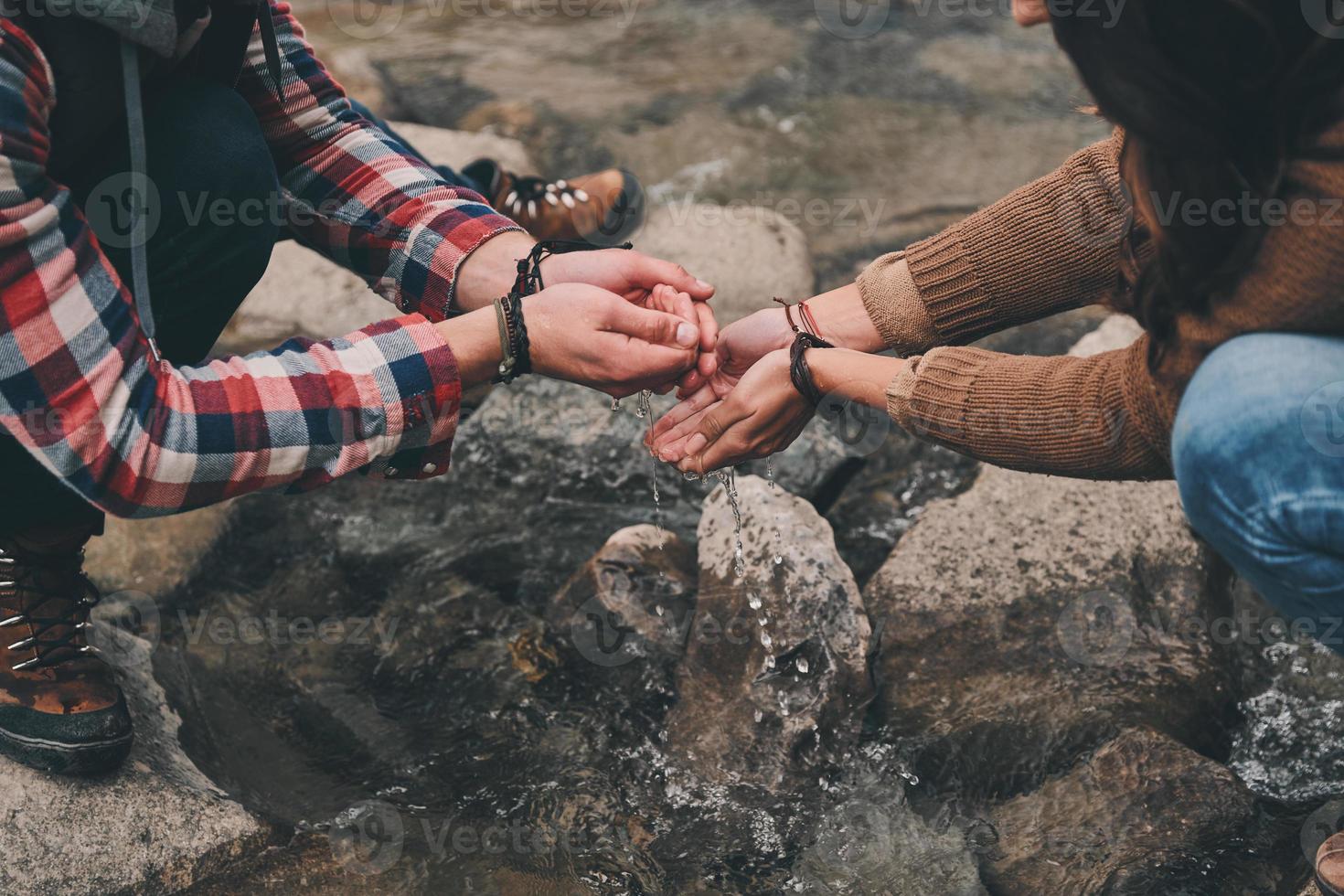 Real refreshment. Close up of young couple washing hands in the river while hiking in mountains photo