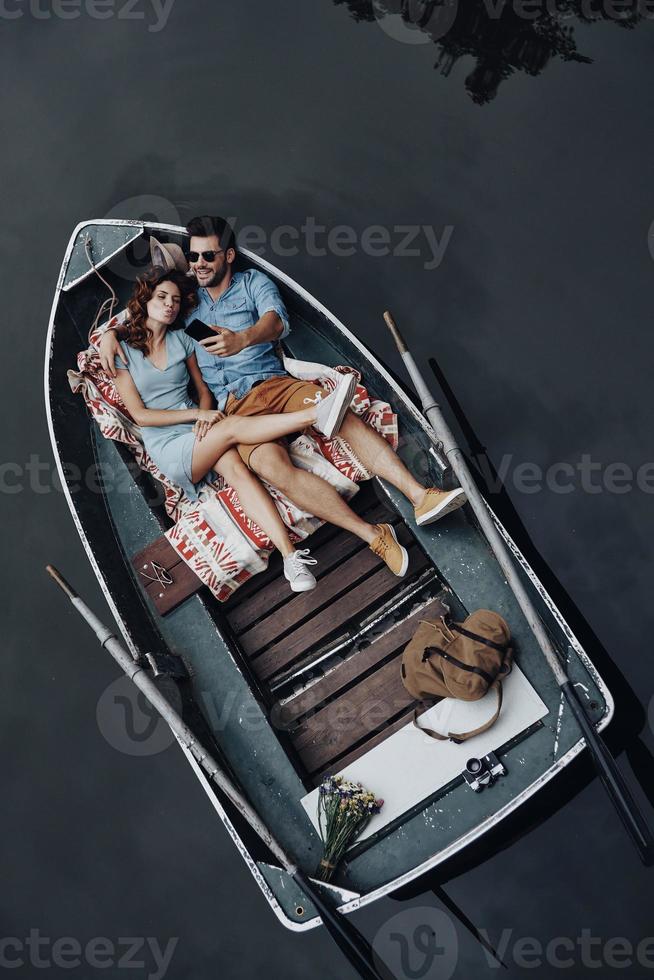 Two hearts full of love. Top view of beautiful young couple taking selfie using smart phone while lying in the boat photo