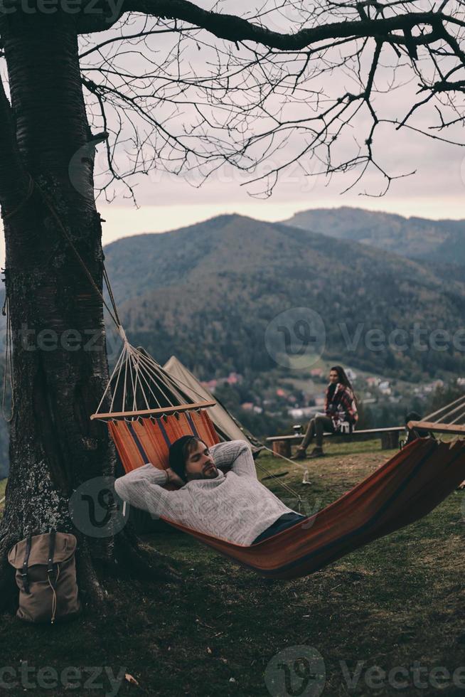 tiempo de descansar. apuesto joven acostado en una hamaca mientras acampa con su novia foto