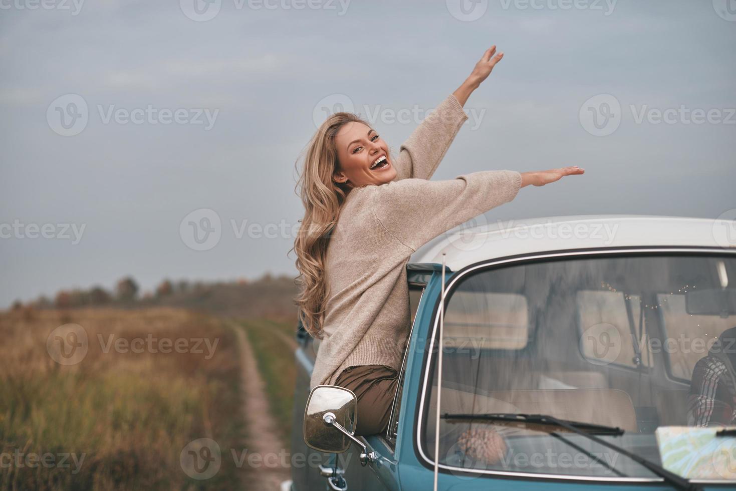 ¿Qué es la vida sin aventuras? Una joven atractiva que se asoma por la ventana de la furgoneta y sonríe mientras disfruta del viaje en coche con su novio. foto