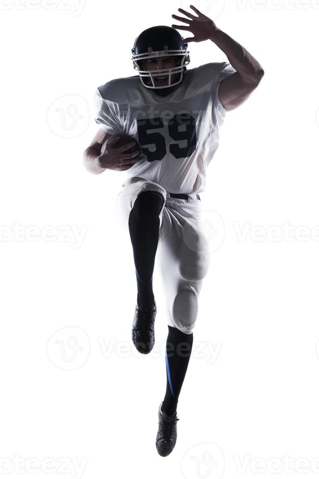 atleta sin miedo. jugador de fútbol americano sosteniendo la pelota y saltando contra el fondo blanco foto