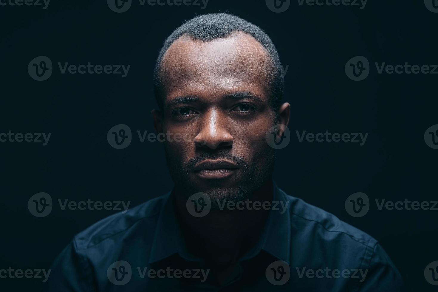 Confident and handsome. Portrait of handsome young African man looking at camera while being in front of black background photo