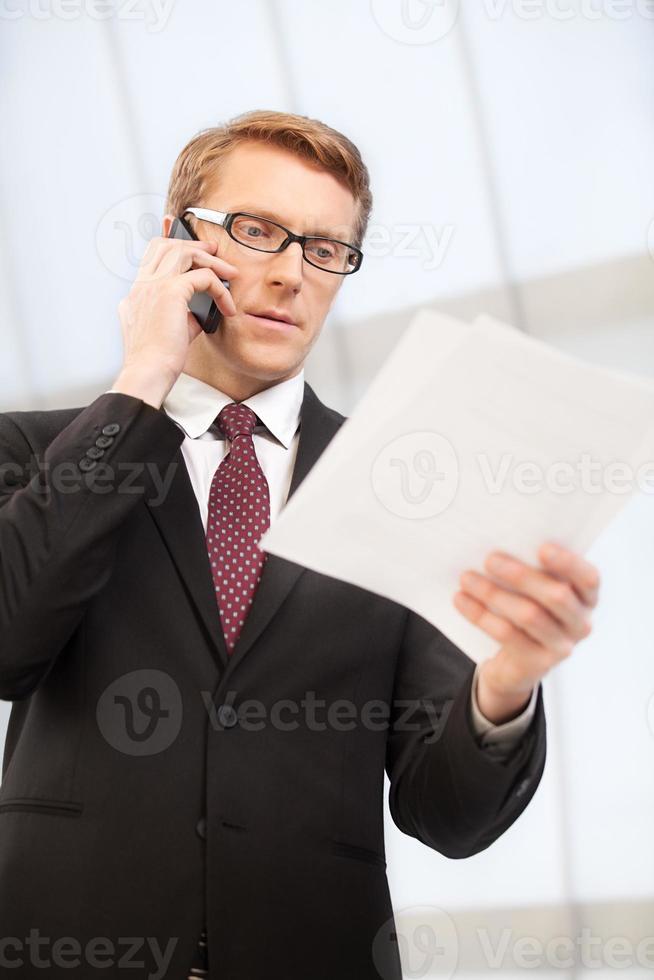 Discussing a report. Confident senior man in formalwear talking on the mobile phone and looking at the documents photo