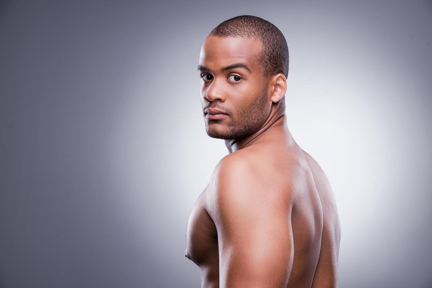 Confident and handsome. Young shirtless African man looking over shoulder while standing against grey background photo