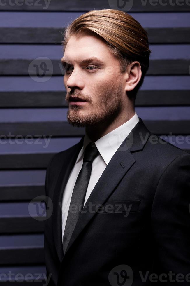 Thoughtful handsome. Side view of handsome young man in formalwear looking away while standing against striped background photo