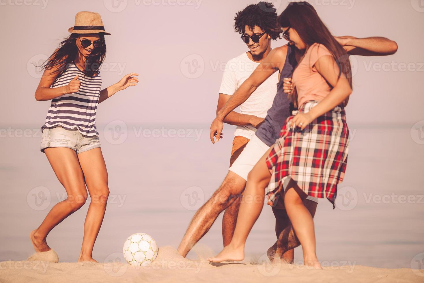 pasar un buen rato en la playa. grupo de jóvenes alegres jugando con una pelota de fútbol en la playa con el mar de fondo foto