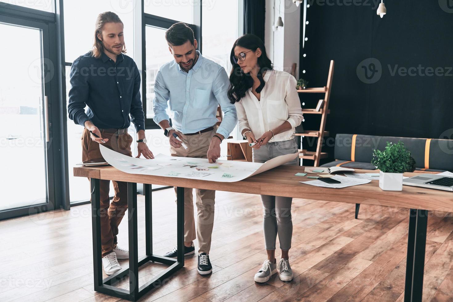 Brainstorming together. Full length of young confident business people discussing something while looking at blueprint in the office photo