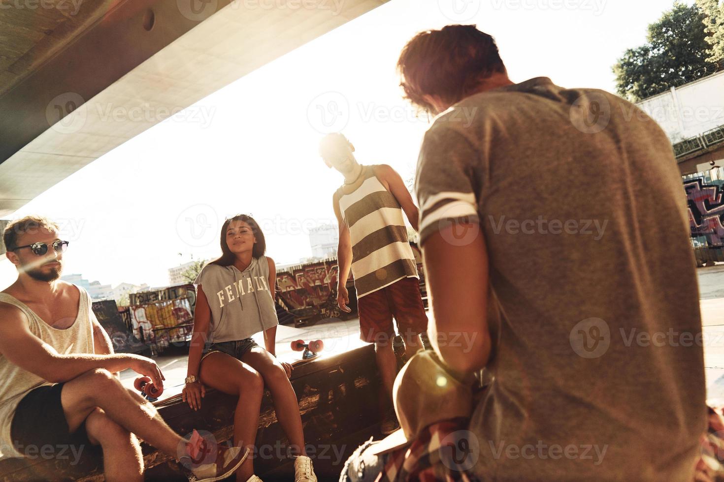 Simply being around. Group of skater friends hanging out together while resting under the bridge outdoors photo