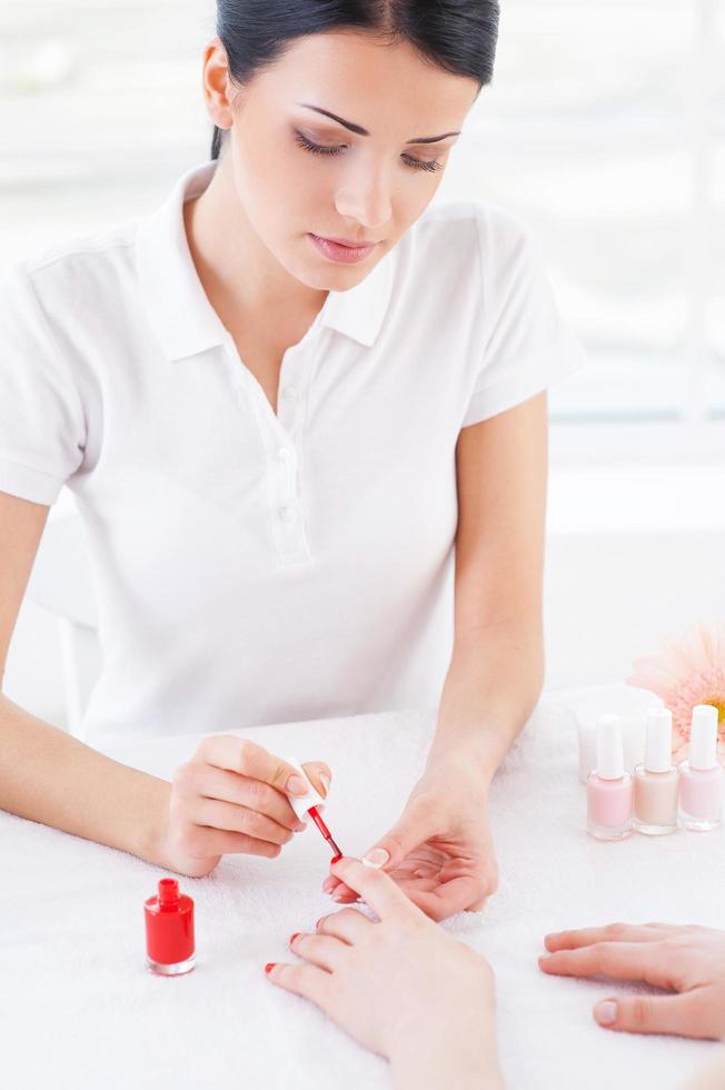 Confident manicurist at work. Top view of beautician doing red manicure to female customer photo