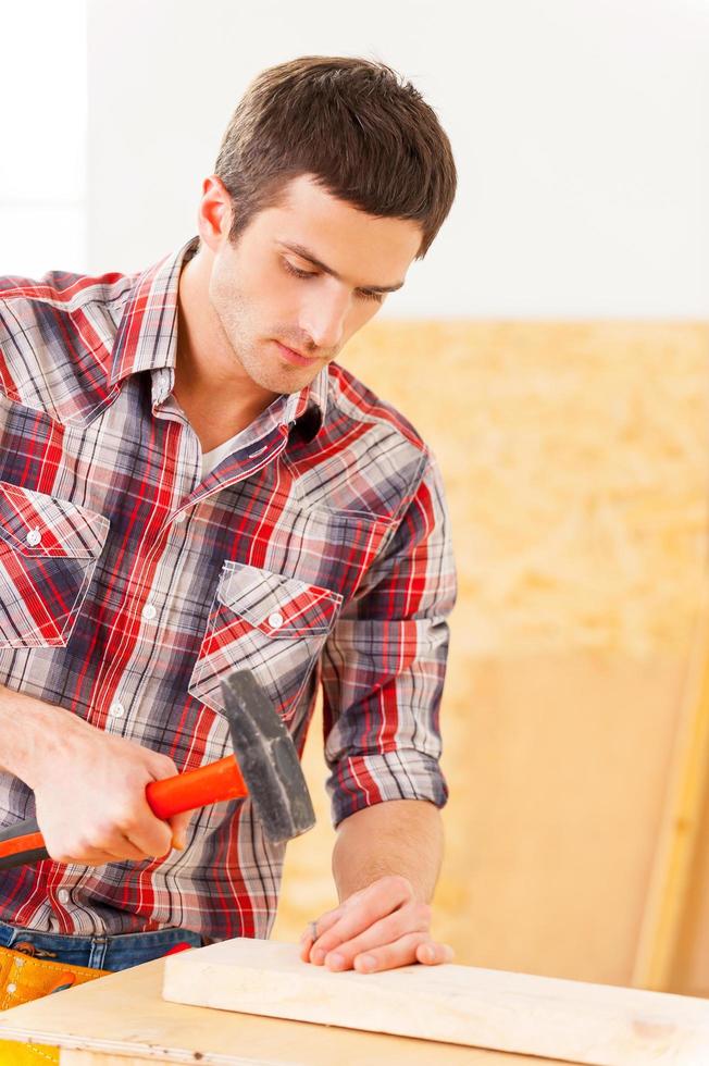 Hammering a nail. Handsome young handyman hammering a nail to a wooden deck photo