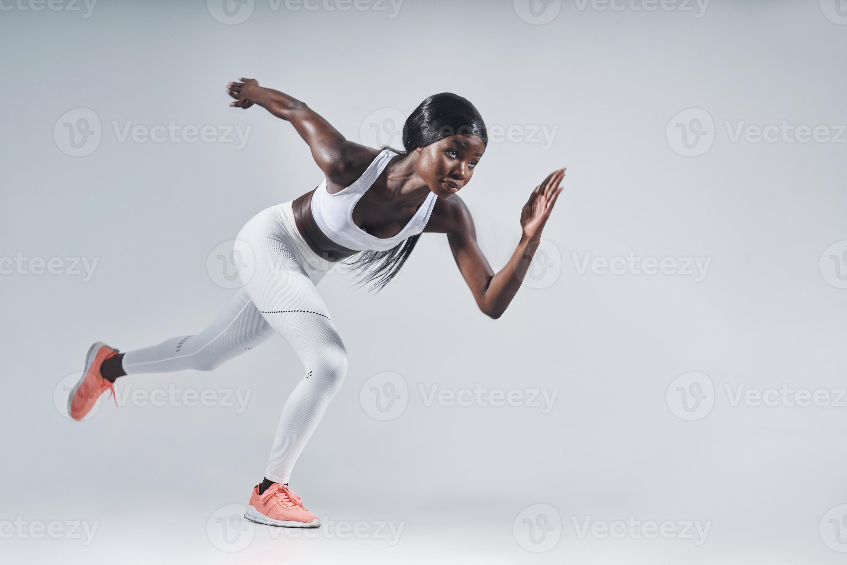 Beautiful young African woman in sports clothing running against gray