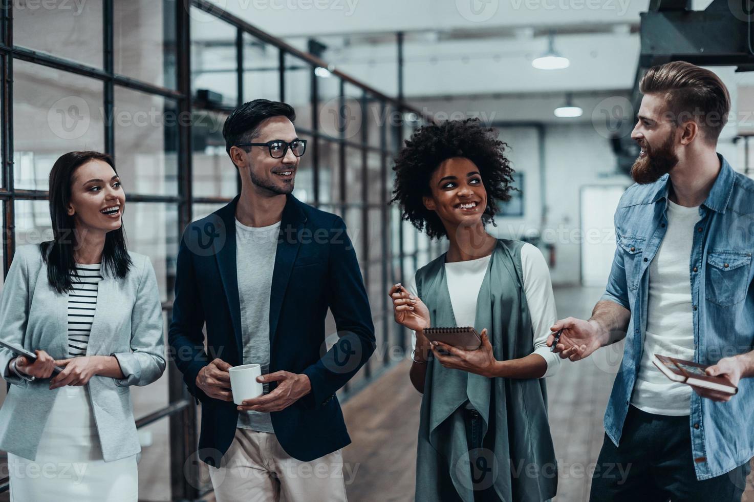 Friendly business chatter. Full length of young colleagues in smart casual wear discussing something while standing in office hallway photo